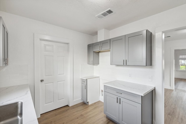 kitchen featuring gray cabinets, light stone countertops, and light hardwood / wood-style flooring