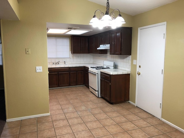 kitchen with white range with gas stovetop, a chandelier, pendant lighting, decorative backsplash, and light tile patterned floors