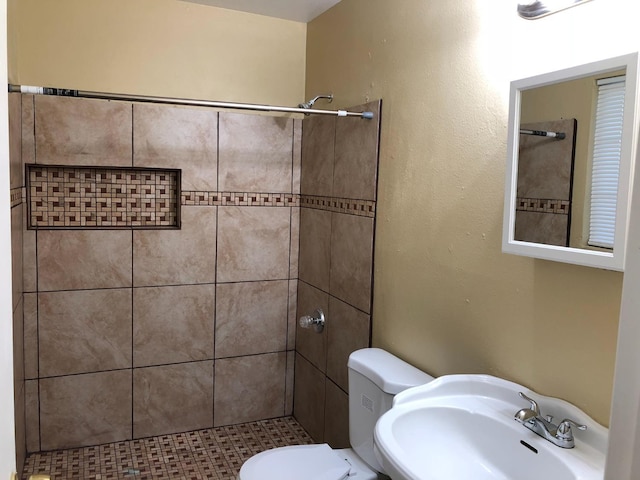 bathroom with a tile shower, sink, and toilet