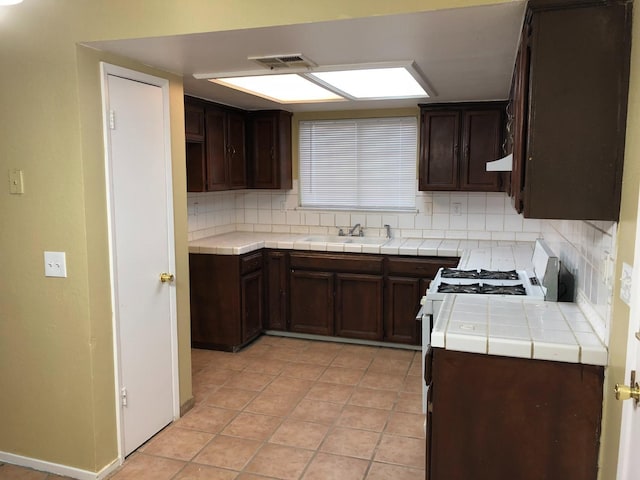 kitchen with decorative backsplash, dark brown cabinets, tile counters, and sink