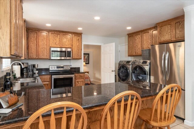 kitchen featuring kitchen peninsula, stainless steel appliances, sink, light tile patterned floors, and washing machine and dryer