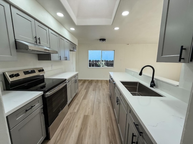 kitchen featuring light stone countertops, sink, light hardwood / wood-style flooring, a tray ceiling, and stainless steel range with electric cooktop