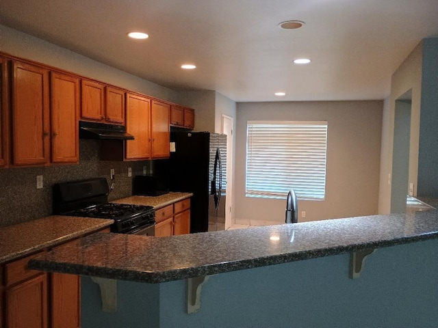 kitchen featuring kitchen peninsula, tasteful backsplash, a breakfast bar area, and black appliances