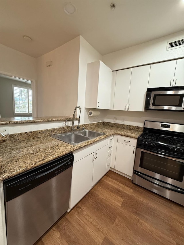 kitchen featuring white cabinetry, sink, stainless steel appliances, kitchen peninsula, and hardwood / wood-style floors