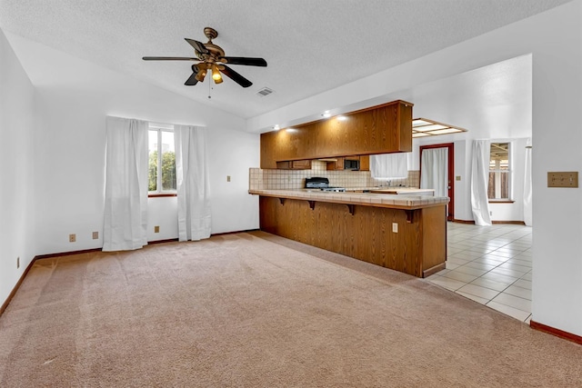 kitchen with tile counters, backsplash, kitchen peninsula, light carpet, and a breakfast bar