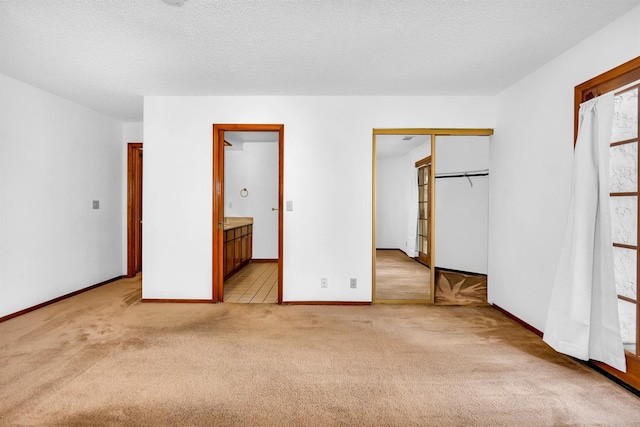 unfurnished bedroom featuring light carpet, a textured ceiling, ensuite bathroom, and a closet