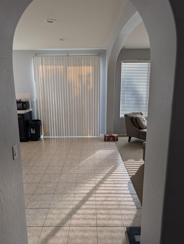 unfurnished room featuring arched walkways, a textured wall, and light tile patterned floors