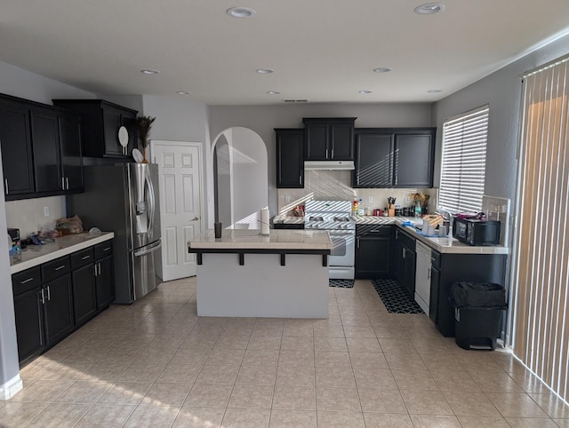 kitchen featuring a breakfast bar area, a kitchen island, light countertops, dark cabinetry, and stainless steel refrigerator with ice dispenser