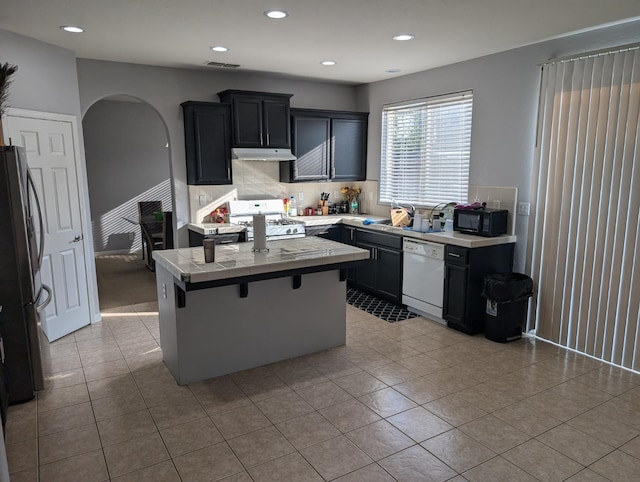 kitchen with white appliances, arched walkways, a kitchen island, light countertops, and under cabinet range hood