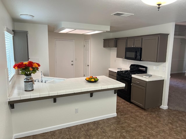 kitchen featuring sink, black appliances, a kitchen bar, tile countertops, and kitchen peninsula