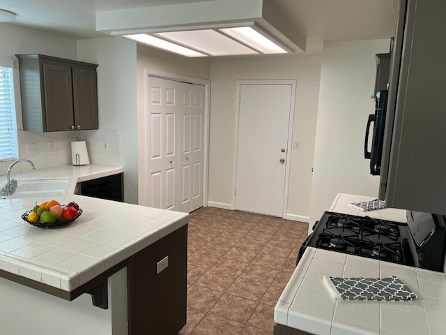 kitchen with sink, tasteful backsplash, gas range, tile countertops, and kitchen peninsula