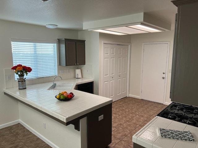 kitchen featuring dark brown cabinetry, sink, tile countertops, a textured ceiling, and kitchen peninsula