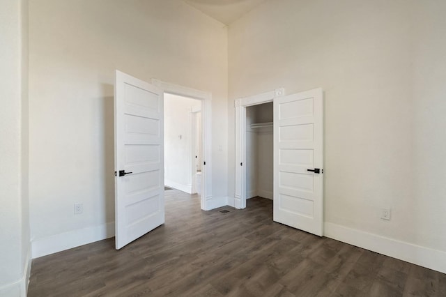 unfurnished bedroom featuring a closet, a towering ceiling, and dark hardwood / wood-style floors