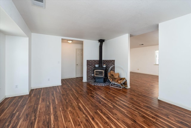 unfurnished living room featuring a wood stove, a textured ceiling, and dark hardwood / wood-style flooring