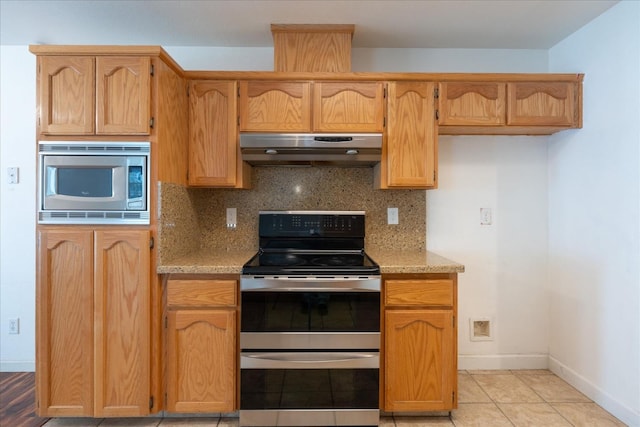 kitchen with stainless steel appliances, light tile patterned floors, light stone counters, and decorative backsplash