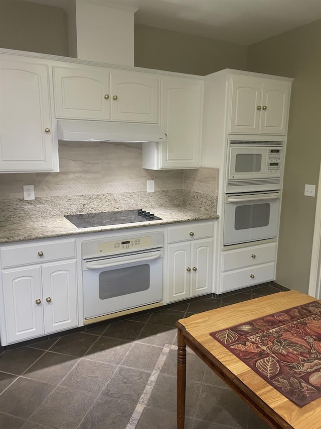 kitchen with white cabinetry, backsplash, dark tile patterned flooring, and white appliances