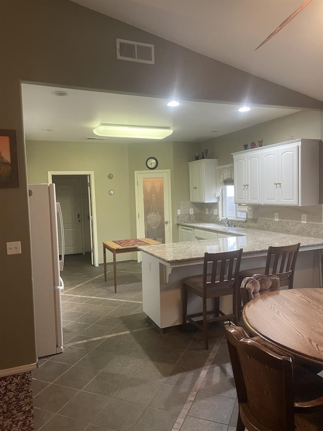 kitchen with white cabinetry, white fridge, kitchen peninsula, vaulted ceiling, and a breakfast bar area