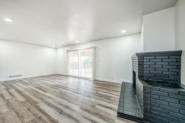 unfurnished living room with hardwood / wood-style flooring and a brick fireplace