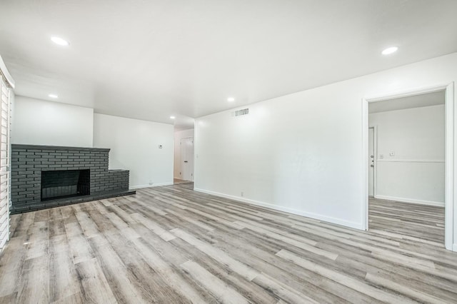 unfurnished living room featuring light hardwood / wood-style floors and a brick fireplace