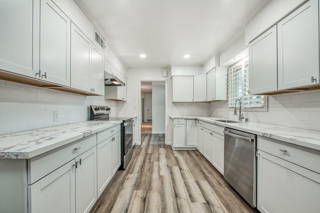 kitchen featuring light stone countertops, white cabinetry, sink, light hardwood / wood-style floors, and appliances with stainless steel finishes