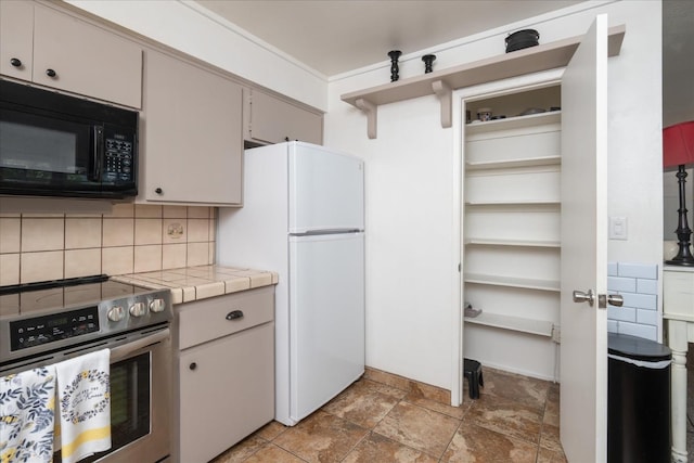 kitchen featuring decorative backsplash, electric range, white fridge, and tile counters