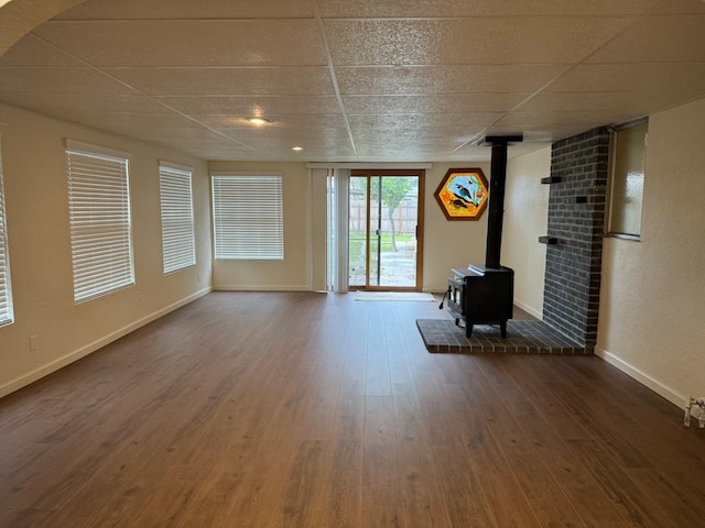 unfurnished living room with hardwood / wood-style floors, a drop ceiling, and a wood stove