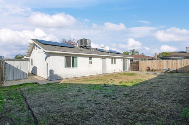 rear view of house featuring central AC unit, a lawn, and solar panels