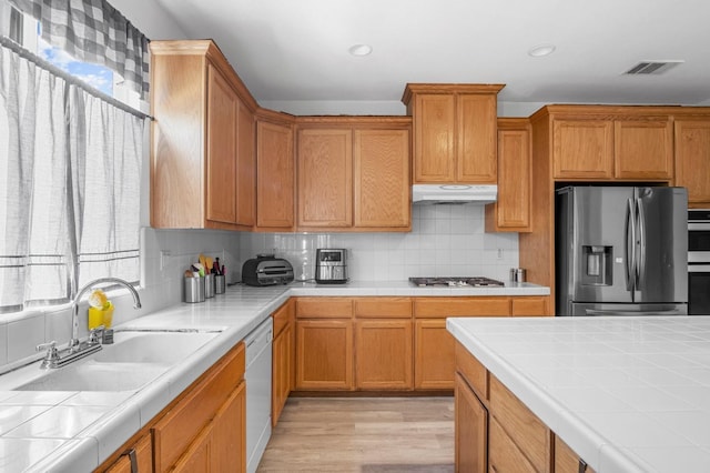 kitchen with tile counters, sink, stainless steel appliances, light hardwood / wood-style floors, and decorative backsplash