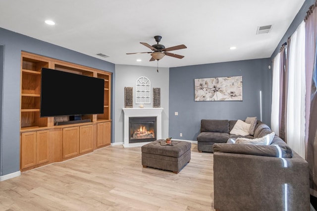 living room with built in shelves, ceiling fan, and light hardwood / wood-style flooring