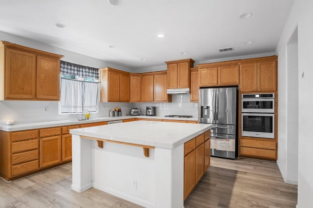 kitchen with tile countertops, a center island, sink, light wood-type flooring, and appliances with stainless steel finishes