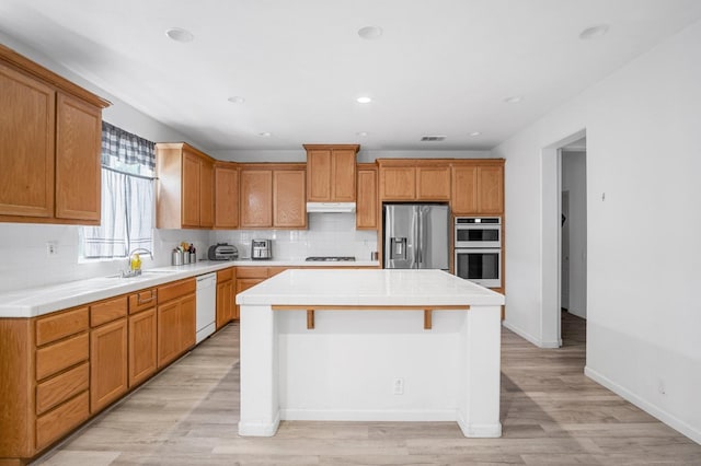 kitchen featuring appliances with stainless steel finishes, a center island, light hardwood / wood-style flooring, and sink