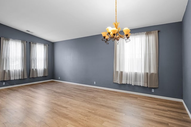 spare room with wood-type flooring, an inviting chandelier, a wealth of natural light, and lofted ceiling