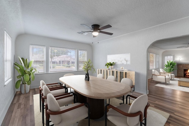 dining space with a fireplace, a textured ceiling, dark hardwood / wood-style flooring, and ceiling fan