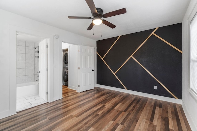 unfurnished room featuring dark wood-type flooring, ceiling fan, and stacked washer and clothes dryer