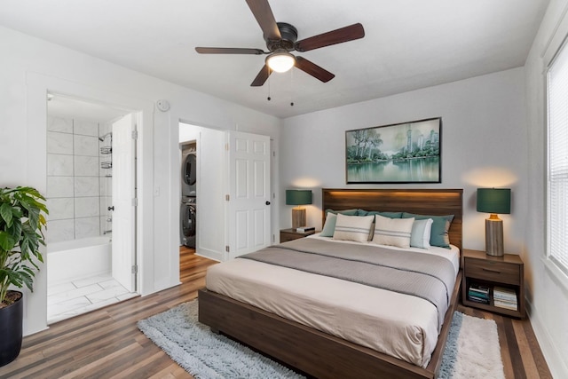 bedroom featuring ensuite bathroom, dark wood-type flooring, ceiling fan, and stacked washing maching and dryer