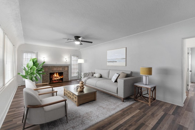 living room with a textured ceiling, ceiling fan, dark hardwood / wood-style flooring, and a fireplace