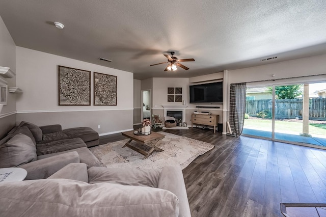 living room with a textured ceiling, ceiling fan, and dark wood-type flooring