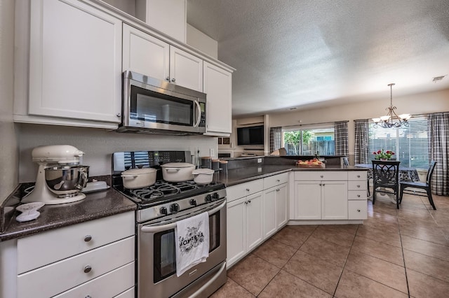 kitchen featuring kitchen peninsula, appliances with stainless steel finishes, decorative light fixtures, an inviting chandelier, and white cabinets