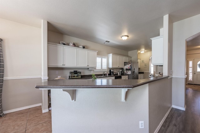 kitchen with white cabinetry, kitchen peninsula, stainless steel refrigerator with ice dispenser, and a breakfast bar area