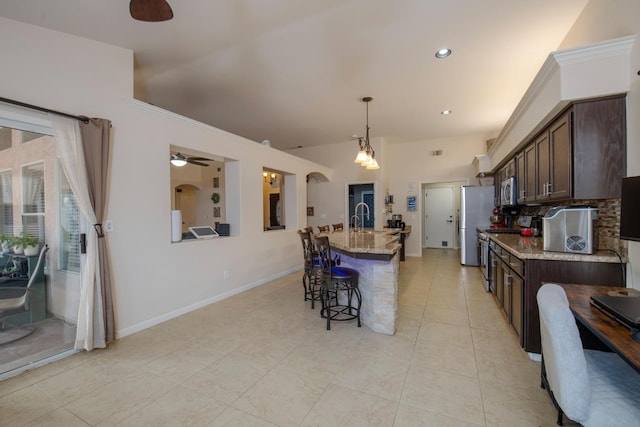 kitchen featuring stainless steel appliances, light stone countertops, dark brown cabinets, and a center island with sink