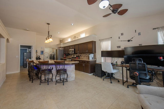 kitchen featuring a kitchen bar, decorative backsplash, dark brown cabinetry, stainless steel appliances, and a center island with sink