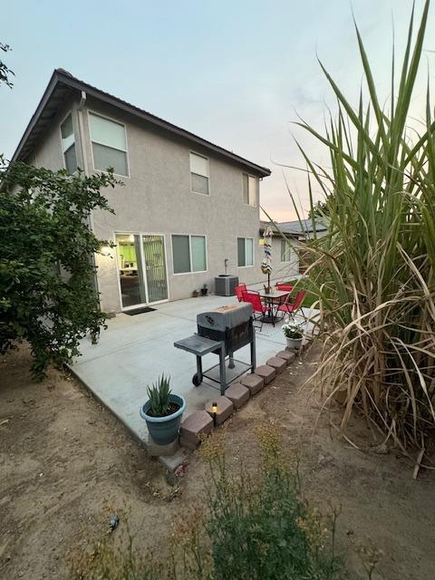 back house at dusk with central AC unit and a patio area