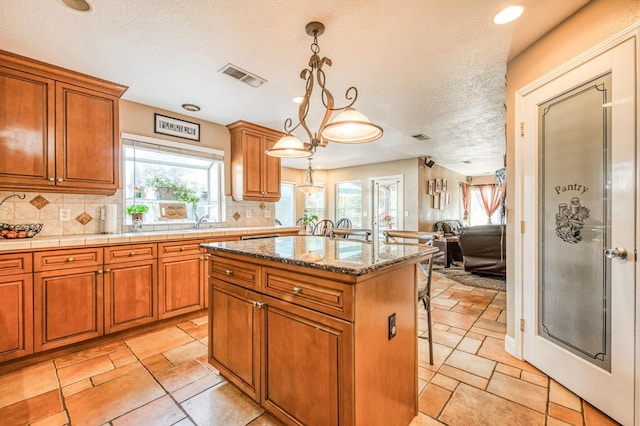 kitchen with a center island, hanging light fixtures, backsplash, a textured ceiling, and a breakfast bar