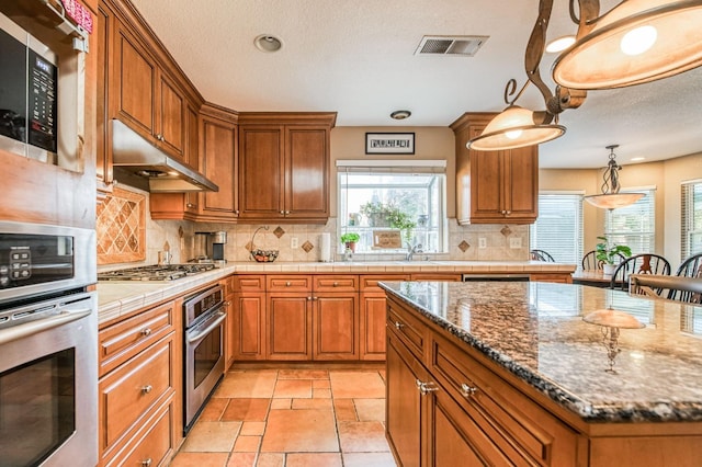 kitchen with a center island, backsplash, stainless steel appliances, and dark stone countertops