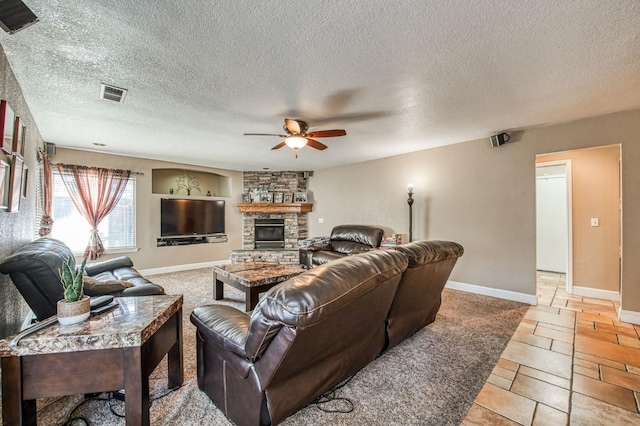 living room with ceiling fan, a stone fireplace, and a textured ceiling