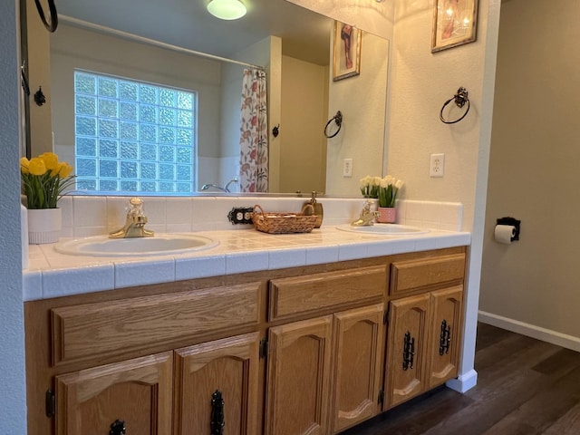 bathroom with double vanity, a sink, baseboards, and wood finished floors