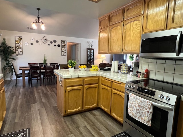 kitchen featuring decorative backsplash, appliances with stainless steel finishes, kitchen peninsula, tile countertops, and a notable chandelier