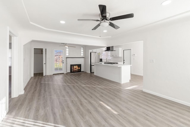 unfurnished living room with ceiling fan, a fireplace, and light wood-type flooring