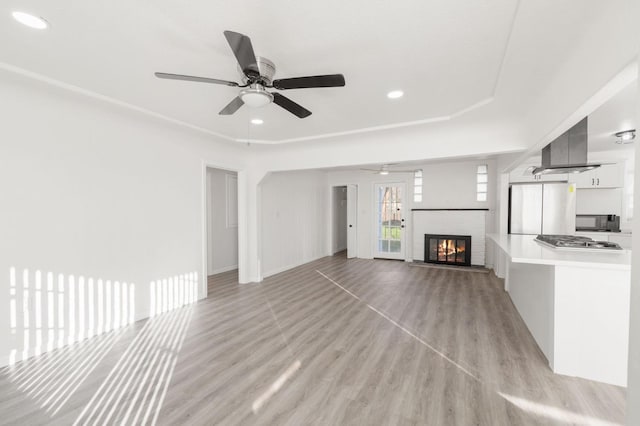 unfurnished living room with ceiling fan, light hardwood / wood-style floors, and a brick fireplace