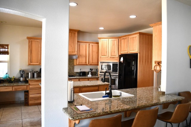 kitchen featuring kitchen peninsula, dark stone countertops, a breakfast bar, light tile patterned floors, and appliances with stainless steel finishes